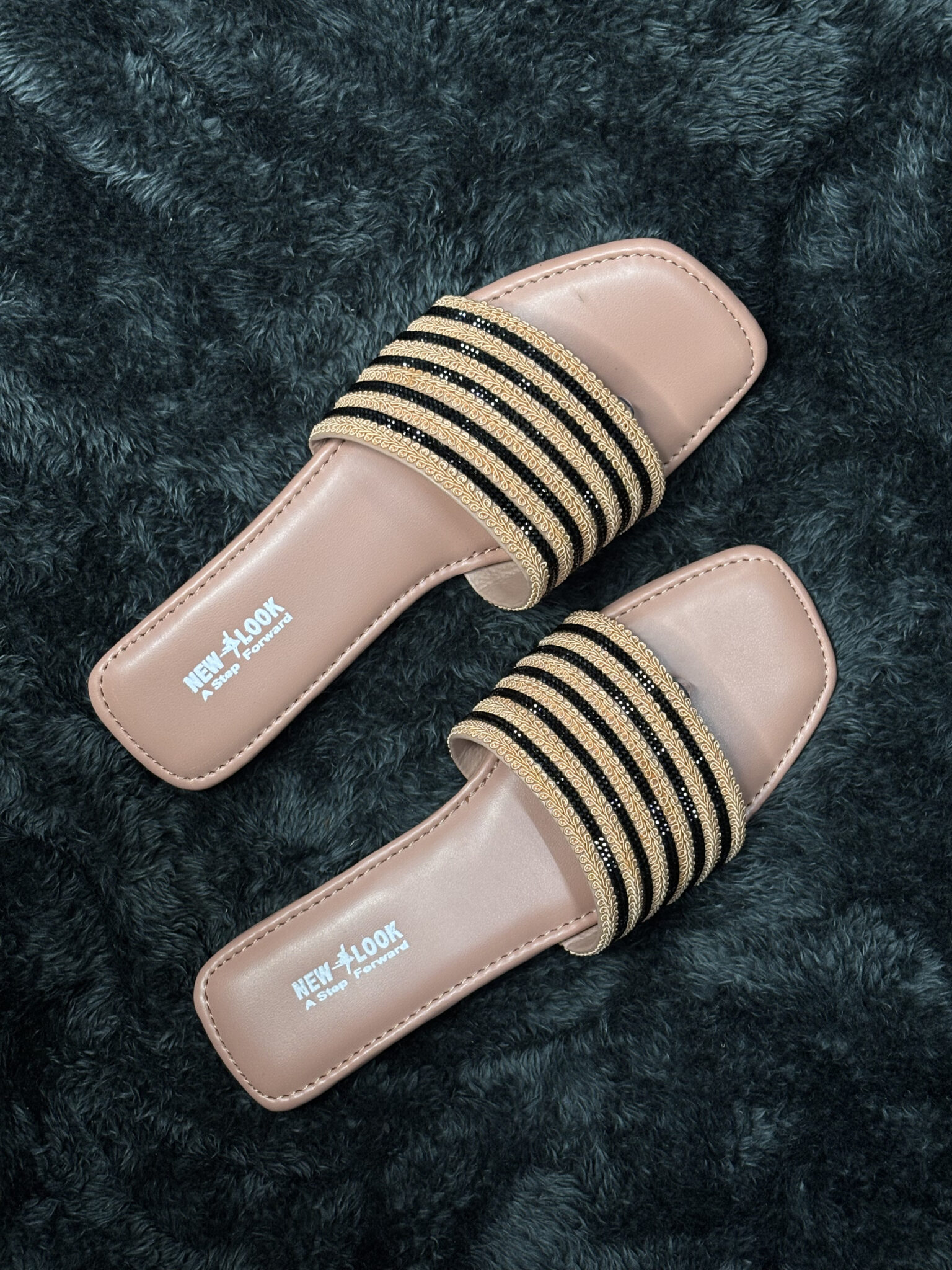 Women’s fancy flat sandals with gold and black accents and a neutral tan base.