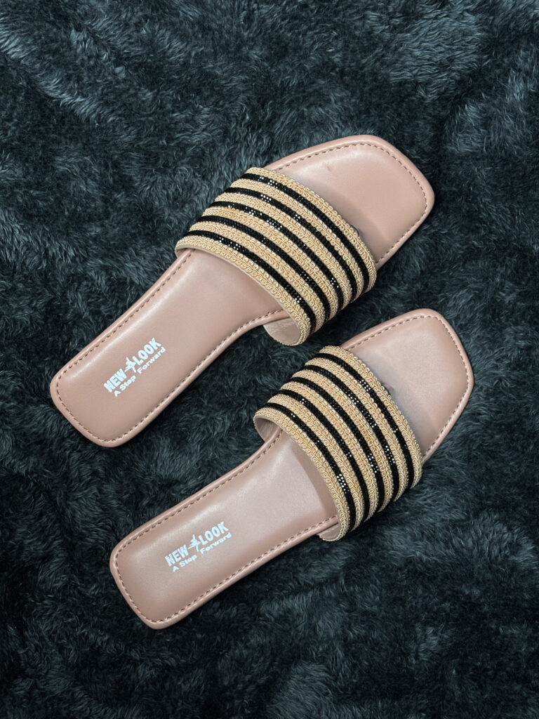 Women’s fancy flat sandals with gold and black accents and a neutral tan base.